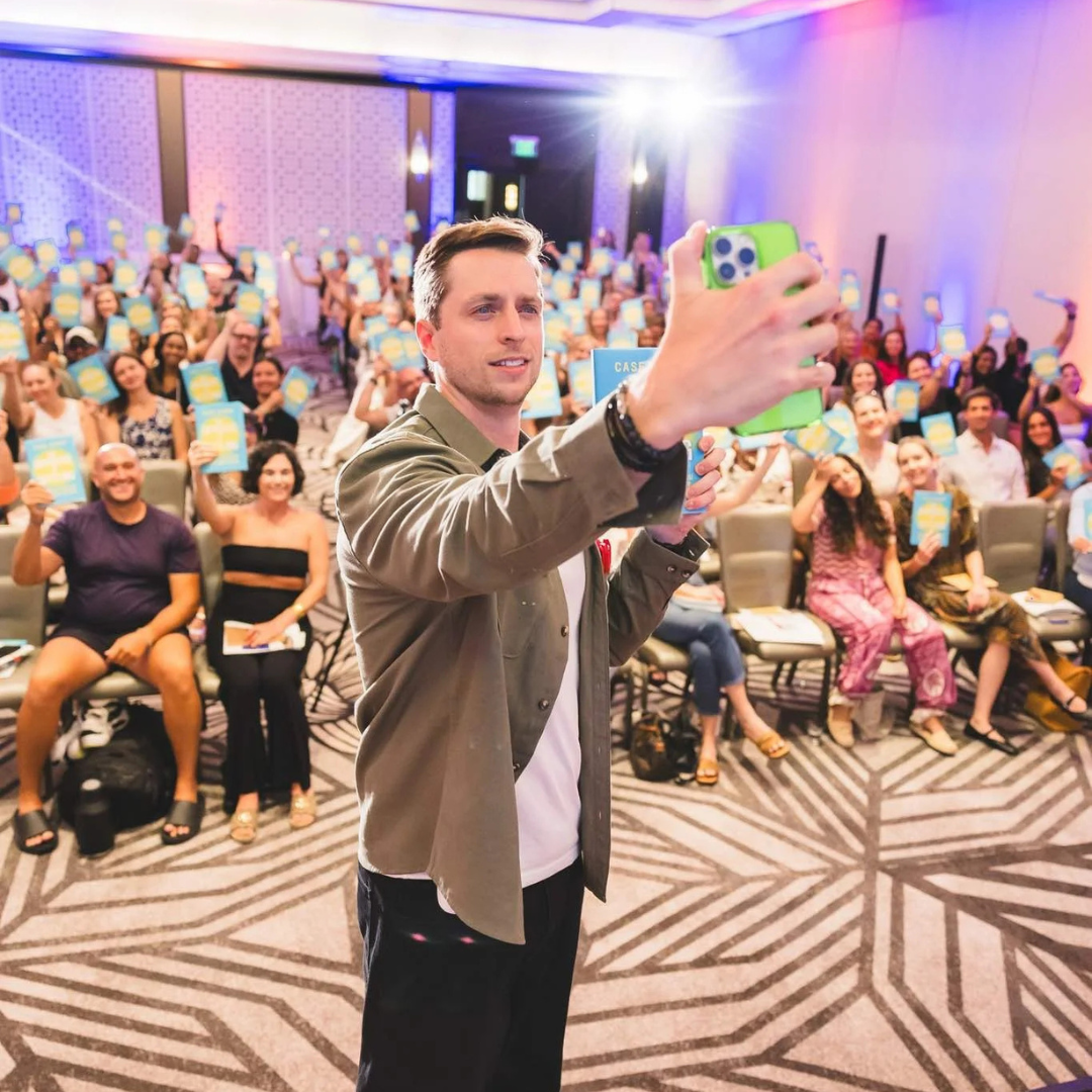 Case Kenny takes a selfie with an enthusiastic audience holding up copies of his book.