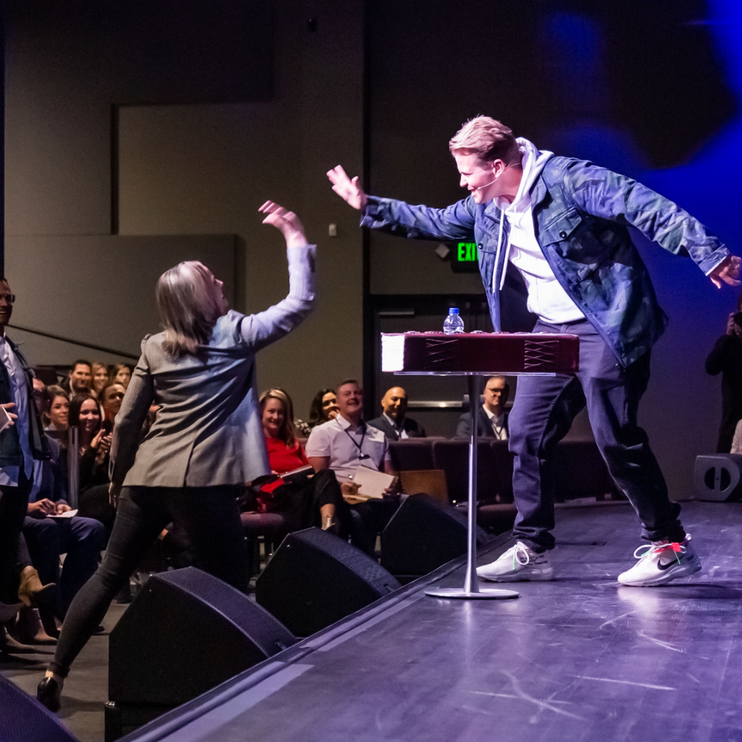 Charlie Rocket high-fives an audience member while speaking on stage.