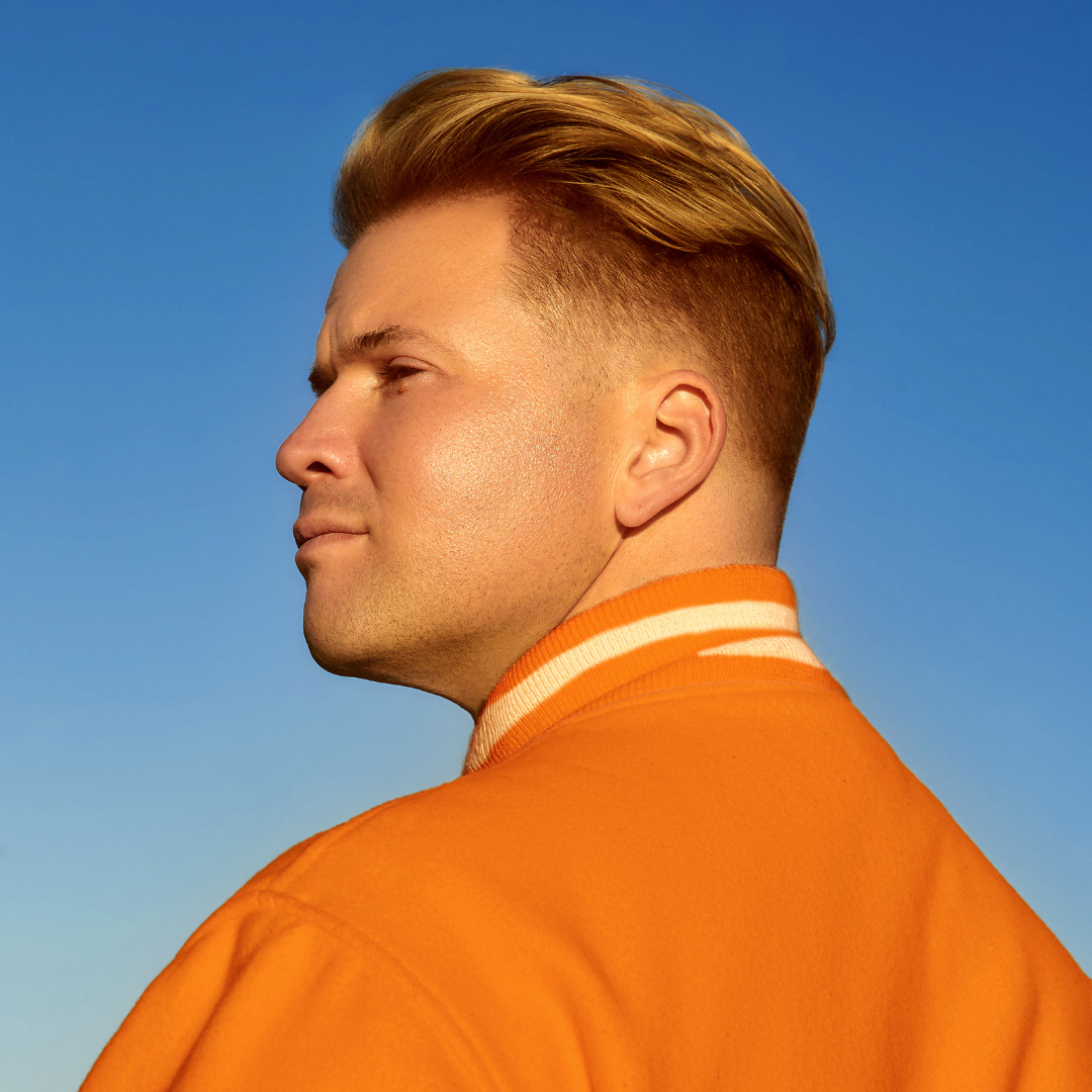 Side-profile portrait of Charlie Rocket wearing an orange jacket against a blue sky.