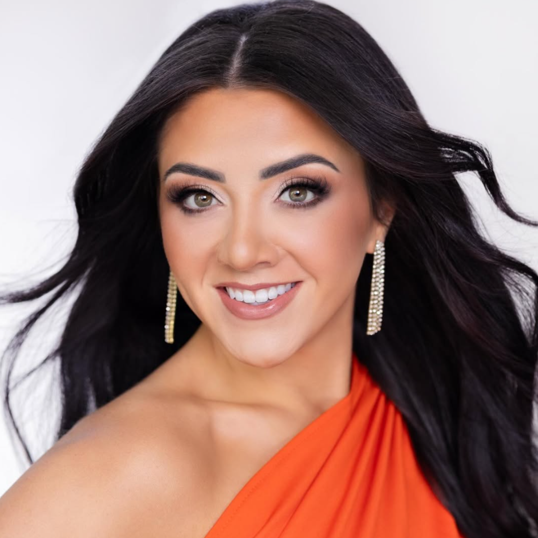 Headshot of Kilie Tomadakis smiling in an orange one-shoulder dress.